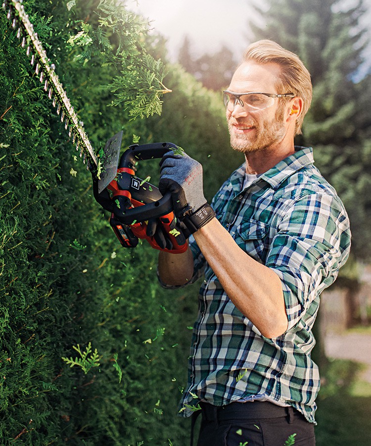 A picture of a man cutting the hedge with a hedge trimmer.