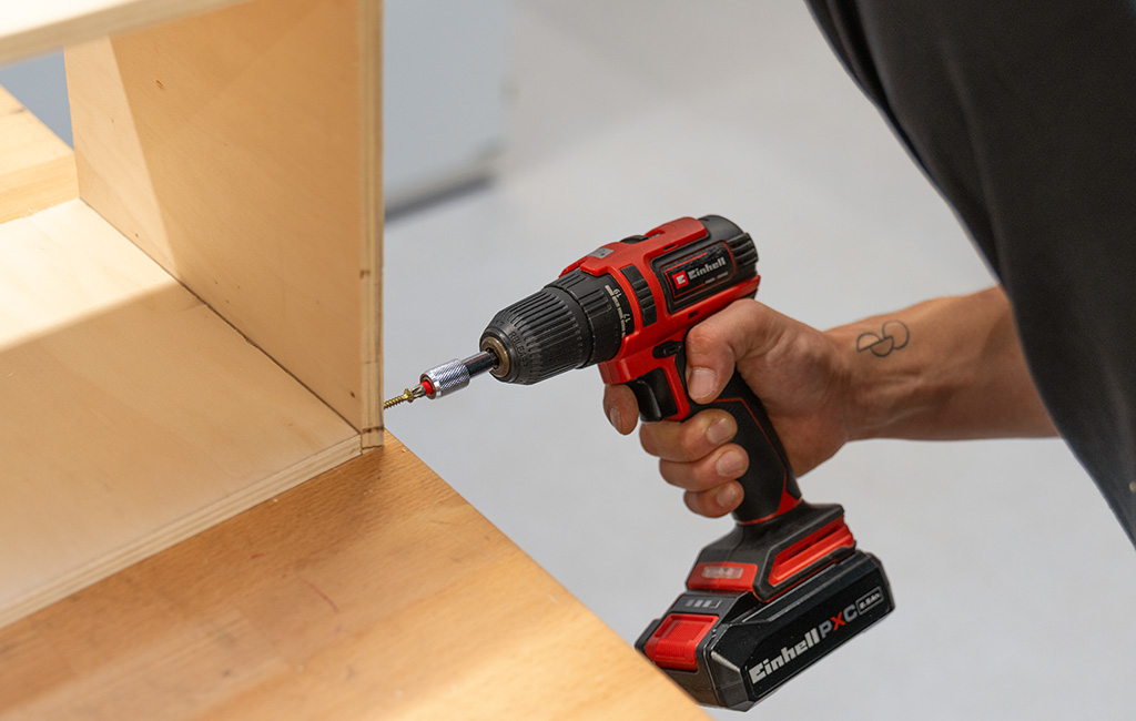 Eine Person bohrt mit einem Akku-Bohrer von Einhell in eine Holzverbindung eines Schranks.