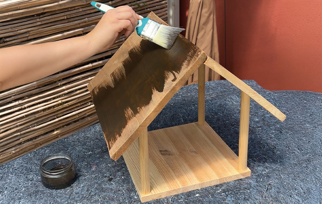 Das Dach des Vogelhauses wird mit einem Pinsel dunkel gestrichen.