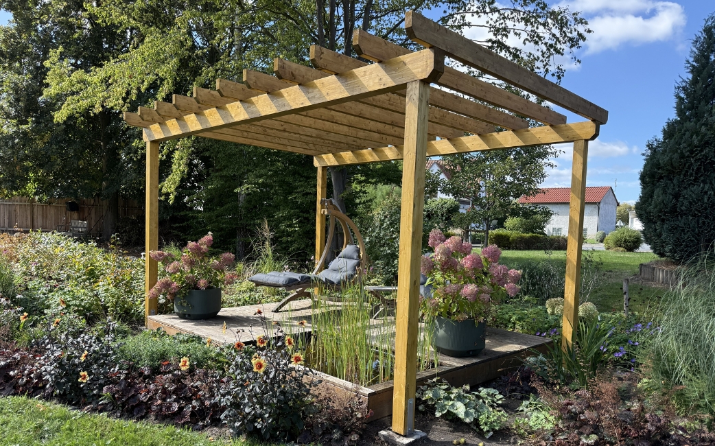 Wooden pergola with a seating area, potted hydrangeas and flowering plants in a garden.