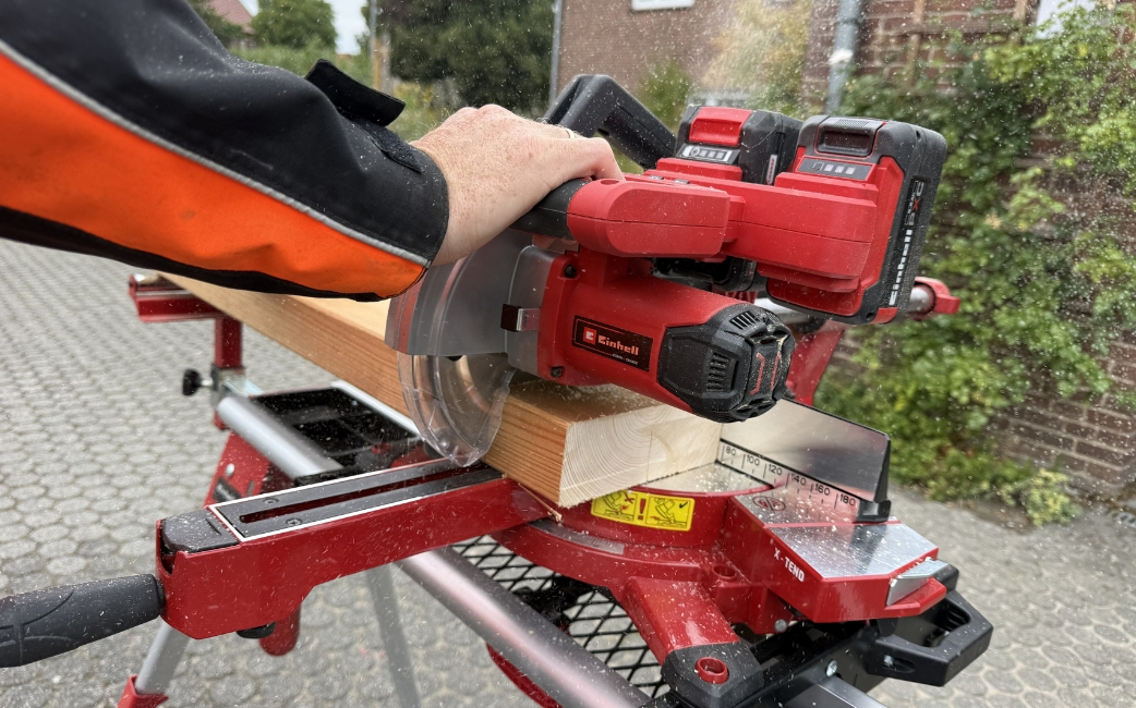 Close-up of a person using a red Einhell sliding mitre saw to cut a wooden beam.