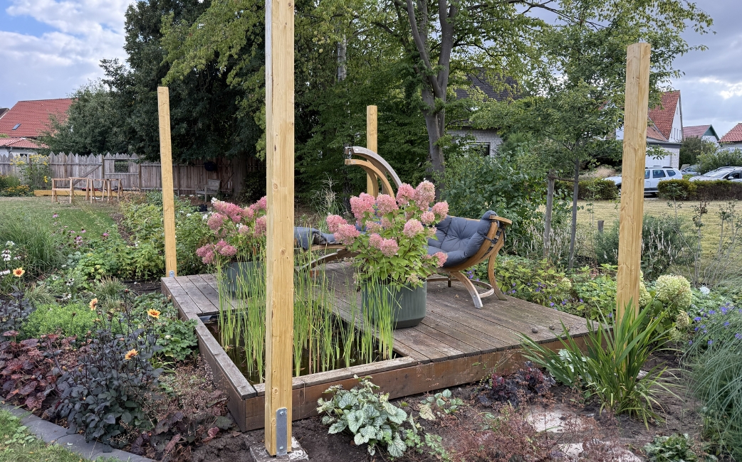 Wooden posts installed on a raised garden platform as the first part of a pergola.