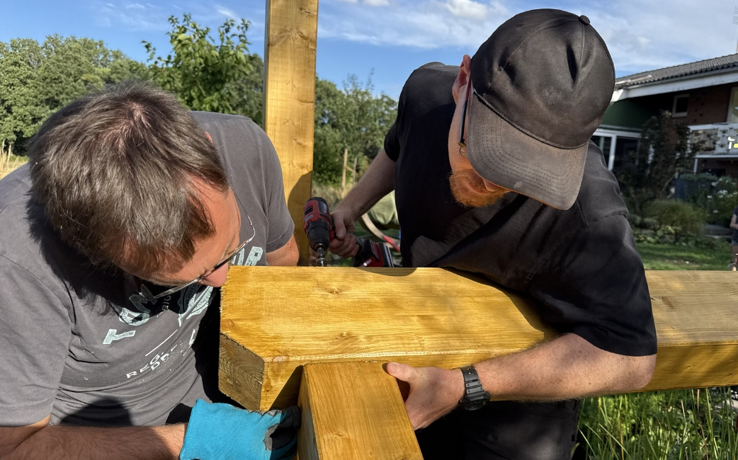 wo people assemble a wooden beam for a garden pergola.