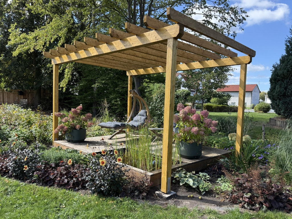 Wooden pergola with a seating area, potted hydrangeas and flowering plants in a garden.