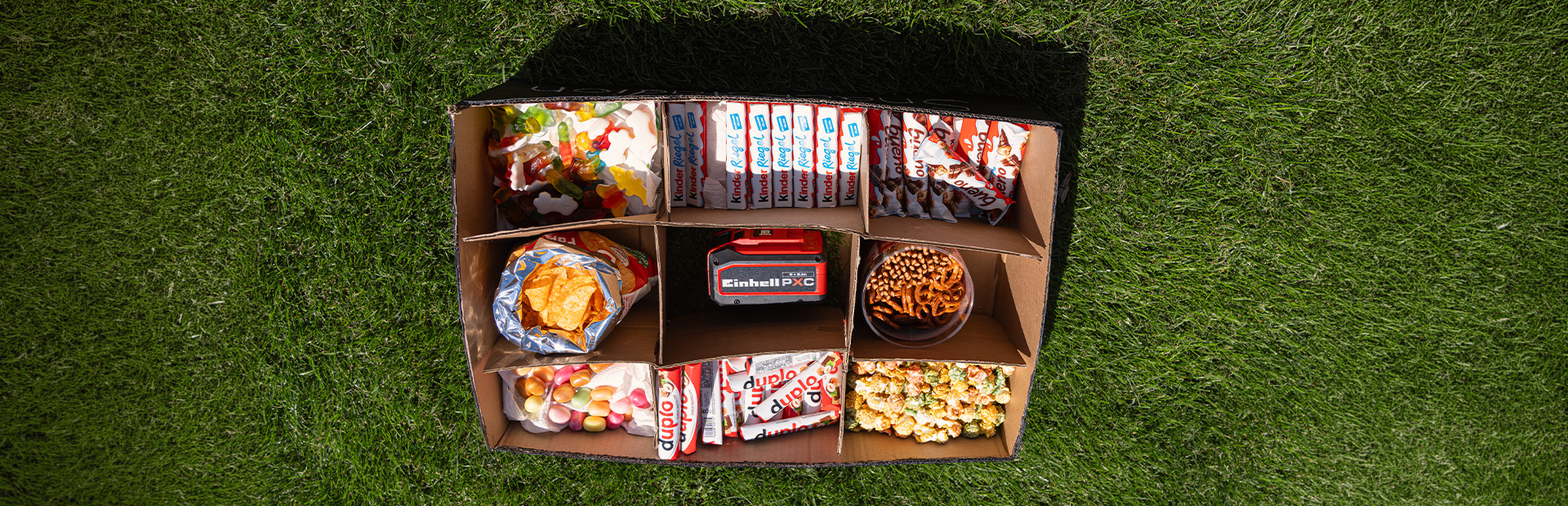 Draufsicht auf Snackbox mit Süßigkeiten, Chips und Brezeln in mehreren Fächern.