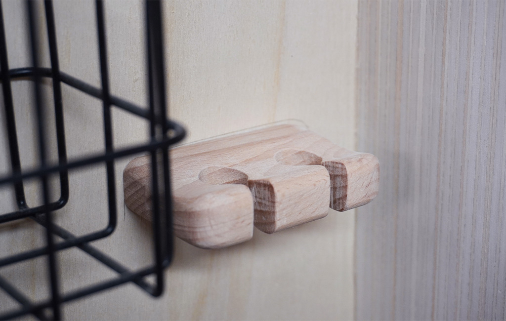 Small wooden holder with cutouts, mounted next to a black wire basket.