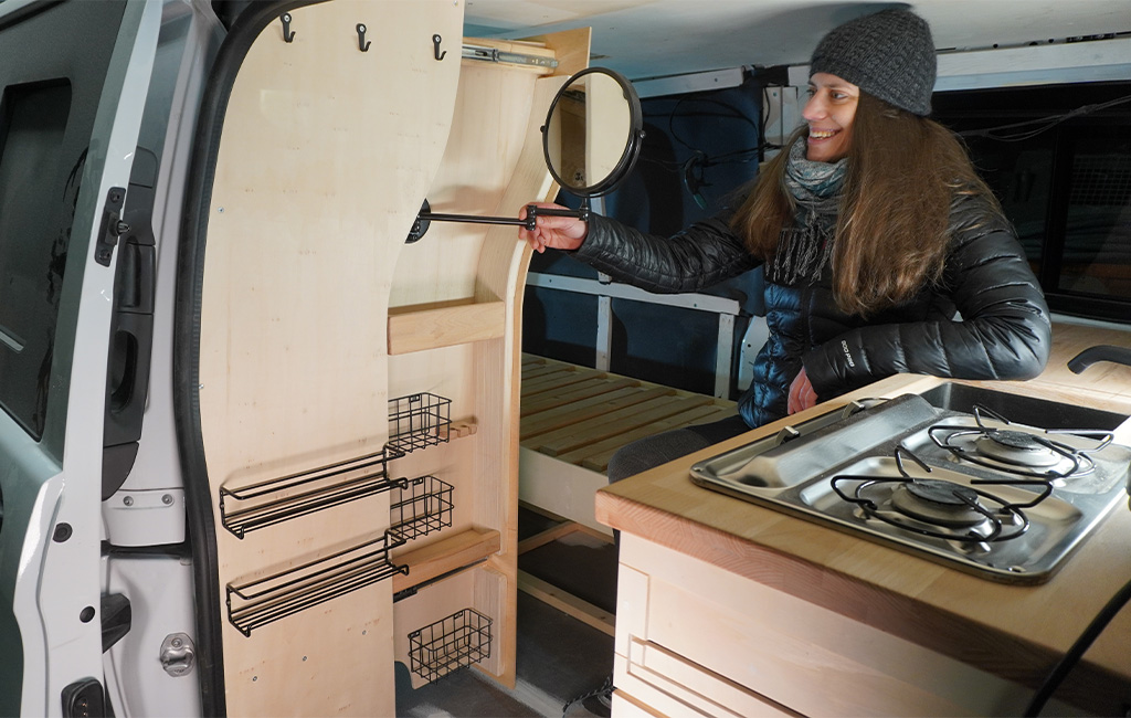 Woman sitting inside the camper smiling while pulling out the mirror from the bathroom cabinet.