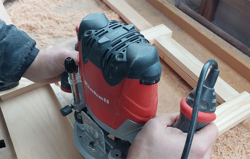 A person is working with an Einhell router on a piece of wood in a workshop.