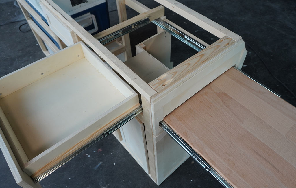 Two extended drawers with rails in a kitchenette under construction, one with a wooden tabletop.