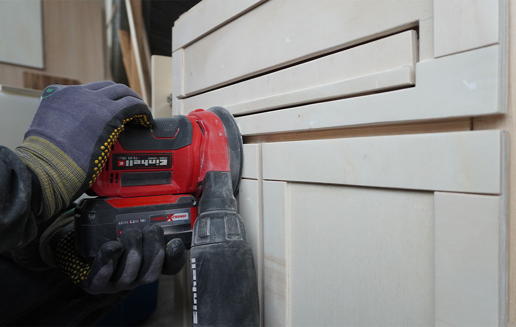 A person sands a cabinet front using an Einhell cordless random orbital sander.