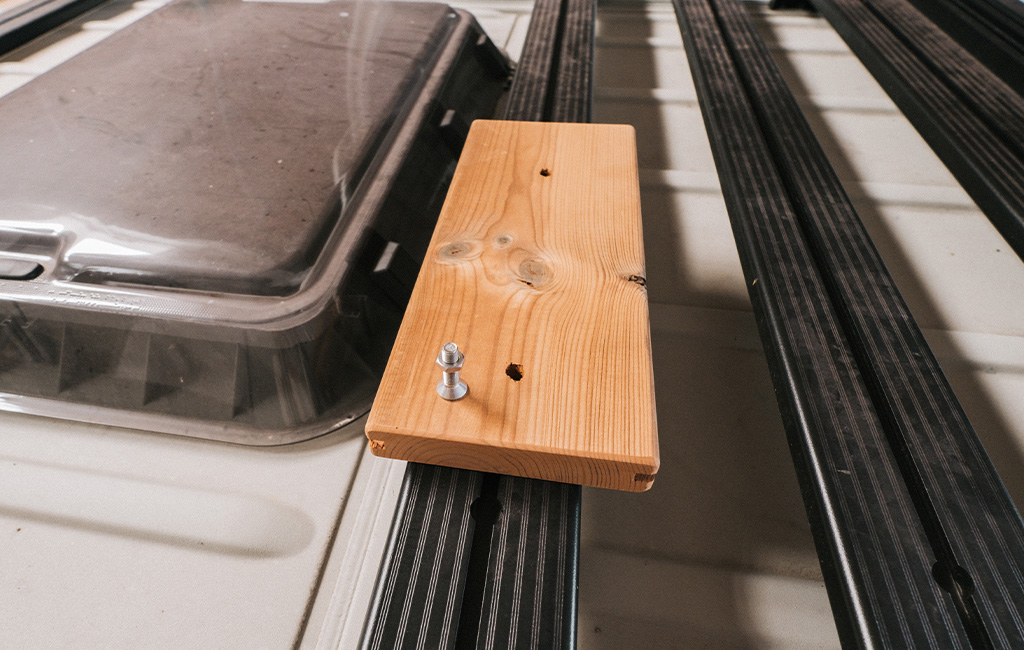 Nahaufnahme eines Holzbretts mit Schrauben auf schwarzem Metallrahmen am Camper-Dach.