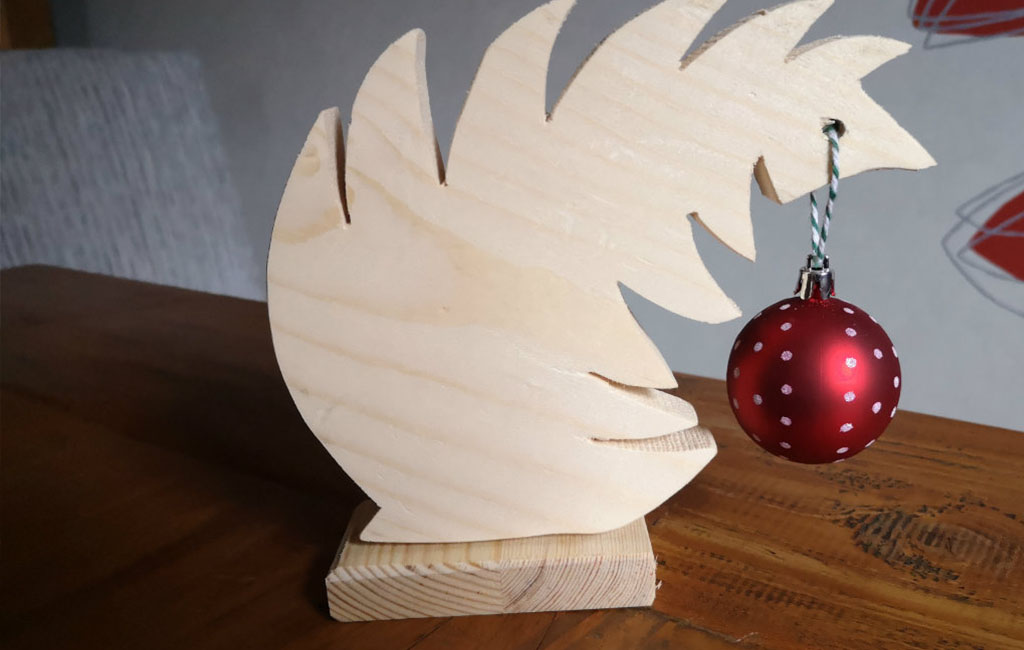 Holzdekoration in Tannenbaumform mit roter Weihnachtskugel.