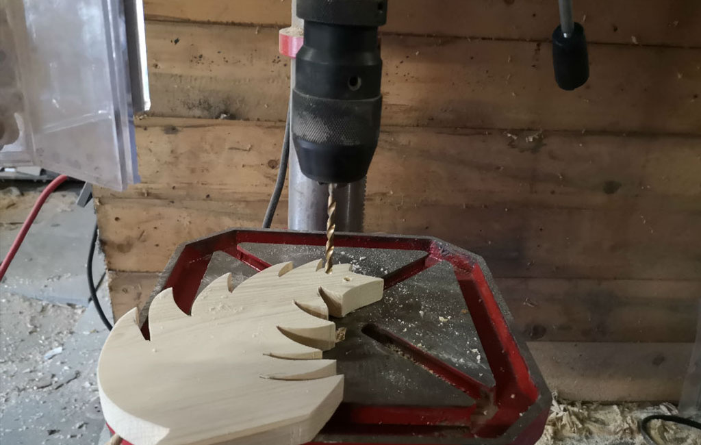 Mit einer Tischbohrmaschine wird ein Loch in einen hölzernen Blattausschnitt für eine DIY-Weihnachtsdekoration gebohrt.
