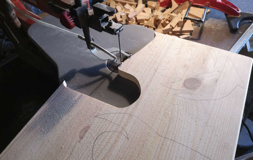 Mit einer Stichsäge wird eine Form aus einem Holzbrett ausgeschnitten.