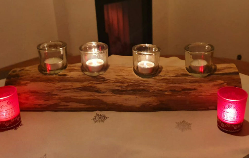 Kerzenhalter aus Holz mit brennenden Teelichtern und roten Kerzen als Weihnachtsdekoration.