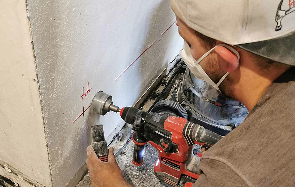 Eine Person bohrt mit einem Bohrer ein Loch in eine Wand, während sich Staub an der Bohrstelle bildet.