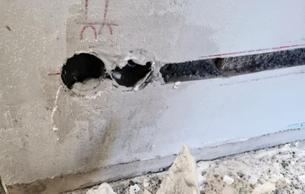 Zwei runde Bohrlöcher und ein Schlitz in einer Wand, darunter Staub und Putzreste.