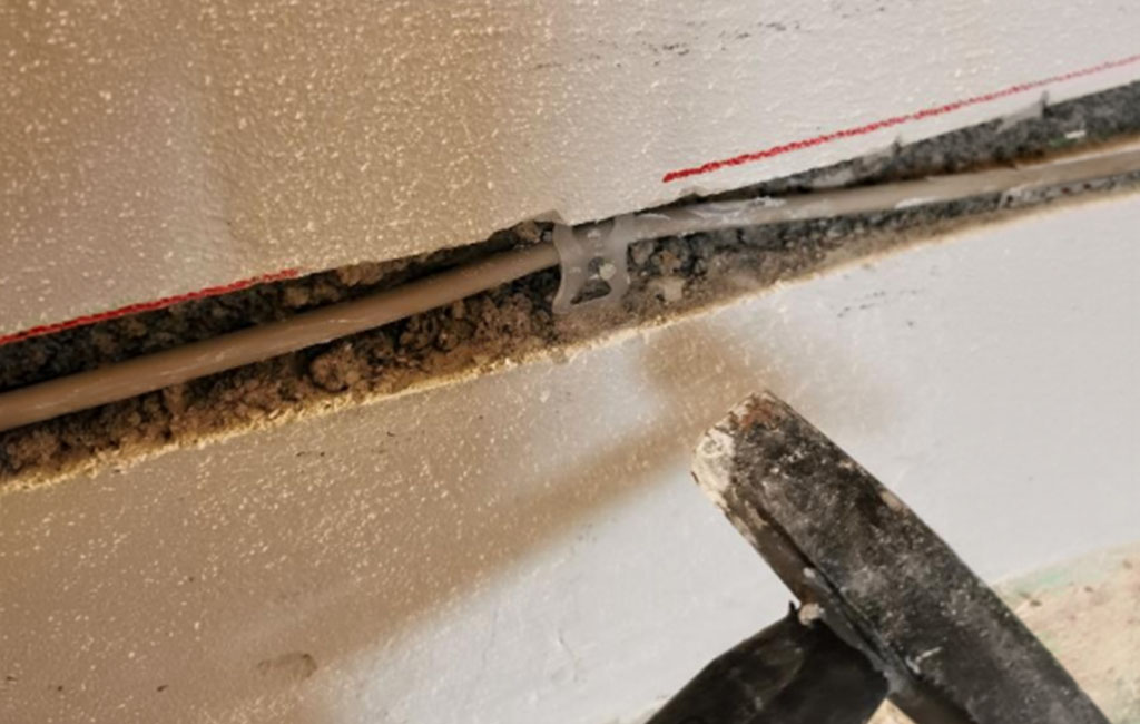 Nahaufnahme einer gefrästen Mauernut, in die ein Kabel verlegt wird, mit Staub und Putzresten entlang der Kante.
