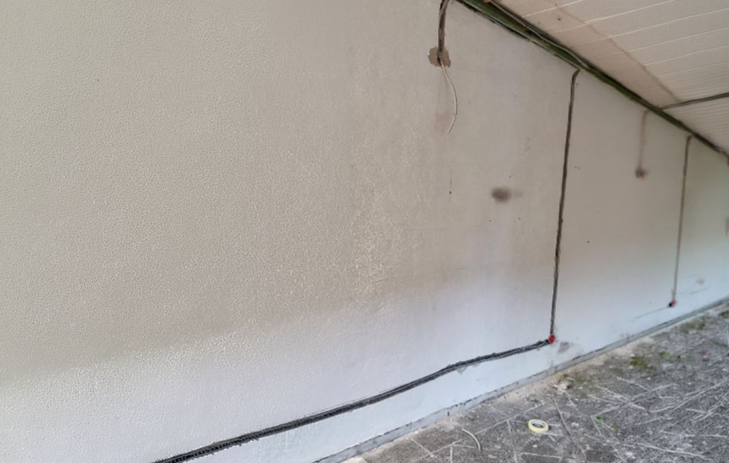 Lange gefräste Mauernut nahe der Decke mit bereits verlegtem Kabel; das herausstehende Kabel wurde abgeschnitten, Staub liegt auf dem Boden.