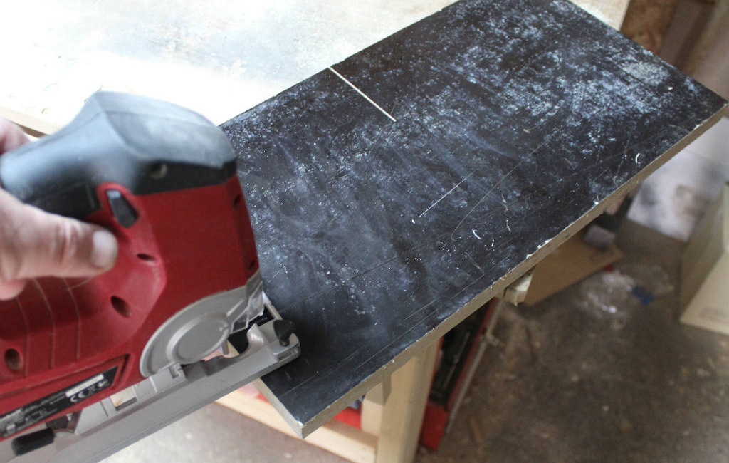 Hand führt Einhell Stichsäge über eine schwarze Platte mit sichtbaren Schnittlinien.