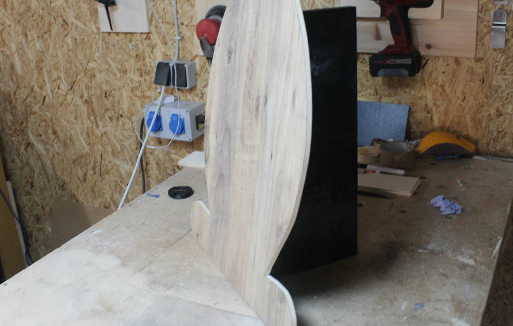 Ausgesägter Holz-Hase steht senkrecht mit schwarzer Stütze in einer Werkstatt.