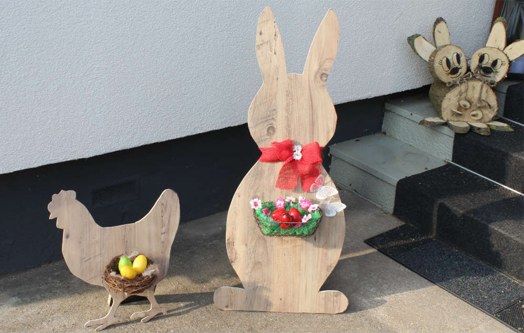 Dekorative Holzfiguren von Hahn und Hase mit Ostereiern vor einer Hauswand.