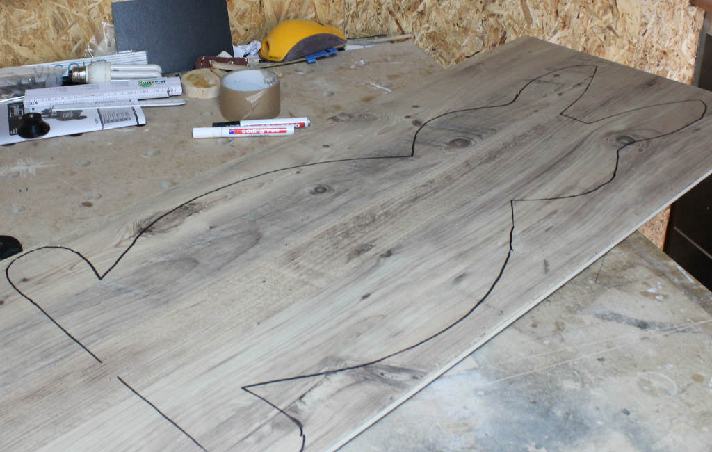 Auf Holzplatte aufgemalte Kontur eines Hasen, mit Marker und Bastelmaterialien daneben.