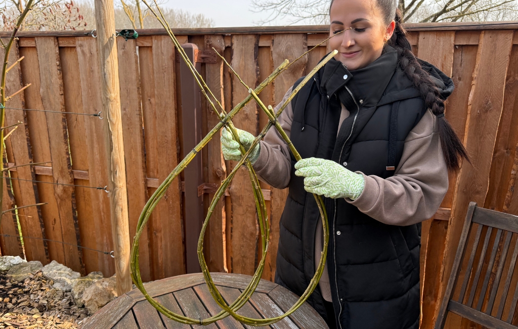 Woman shaping a large wreath from branches over a garden table.
