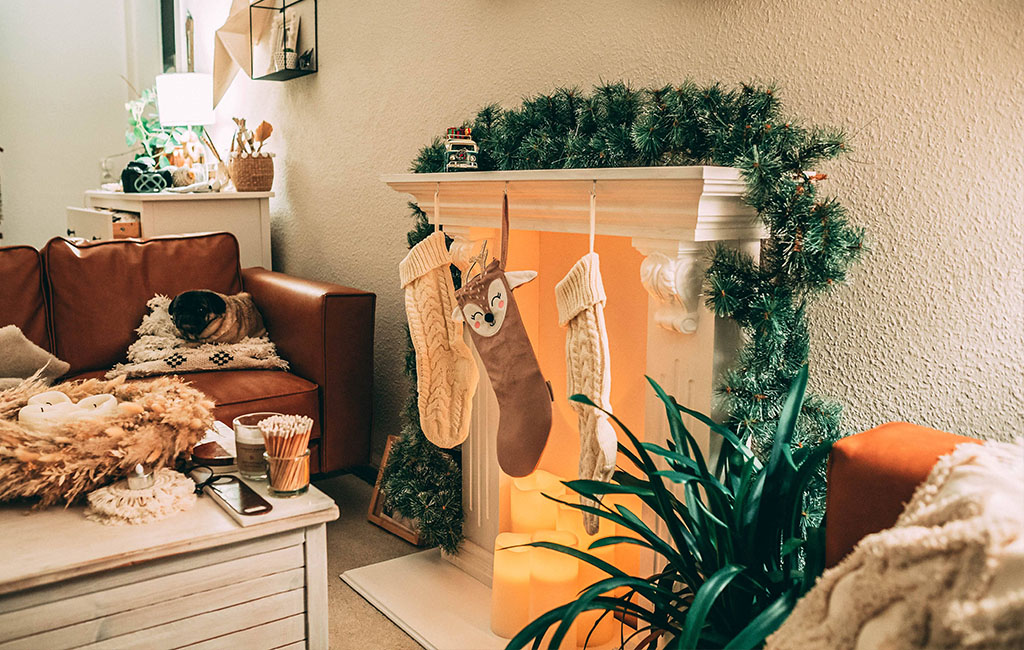 Christmas-themed living room with a decorative fireplace, stockings, lights, and a dog resting on the couch.