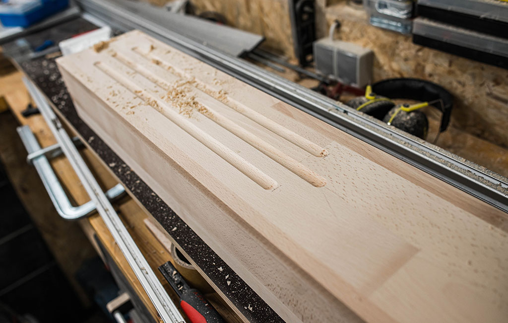 Close-up of a wooden board with elongated routed grooves on a workbench.
