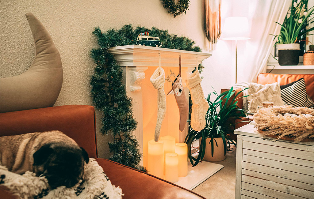 Christmas-decorated living room with faux fireplace, LED candles, stockings, and a sleeping pug on the couch.