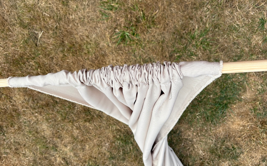 Close-up of gathered beige fabric threaded onto a round wooden rod.