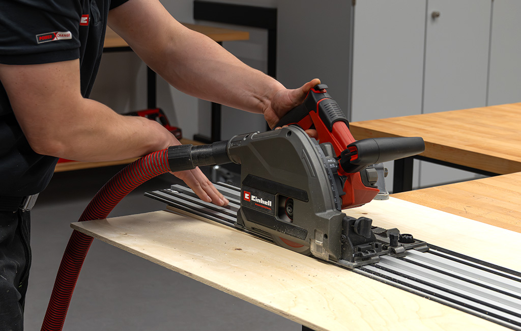 Eine Einhell Tauchsäge wird entlang einer Führungsschiene geführt, um eine Holzplatte gerade zuzuschneiden.
