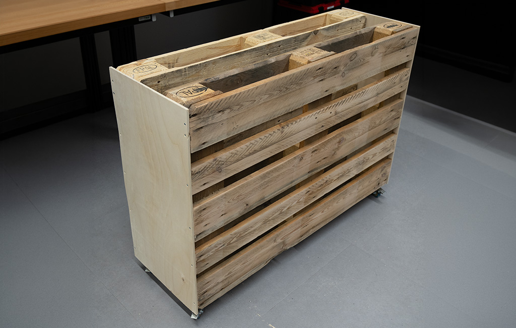 Die Europalette steht auf Rollen und ist an beiden schmalen Seitenwänden mit hellen Holzplatten verkleidet.