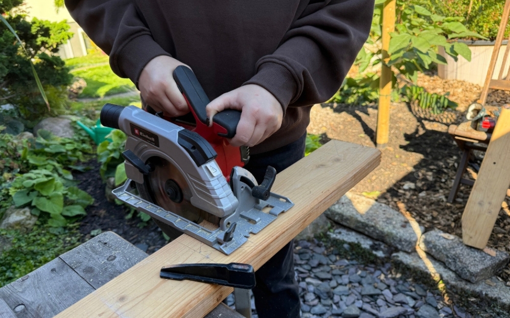 Eine Person führt eine Einhell Handkreissäge und schneidet damit ein Holzbrett.
