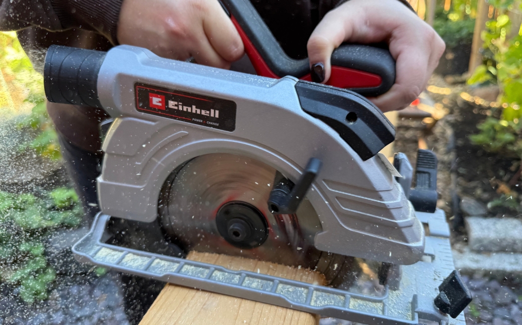 Nahaufnahme einer Einhell-Kreissäge, die ein Holzbrett zersägt, wobei Sägespäne durch die Luft fliegen.