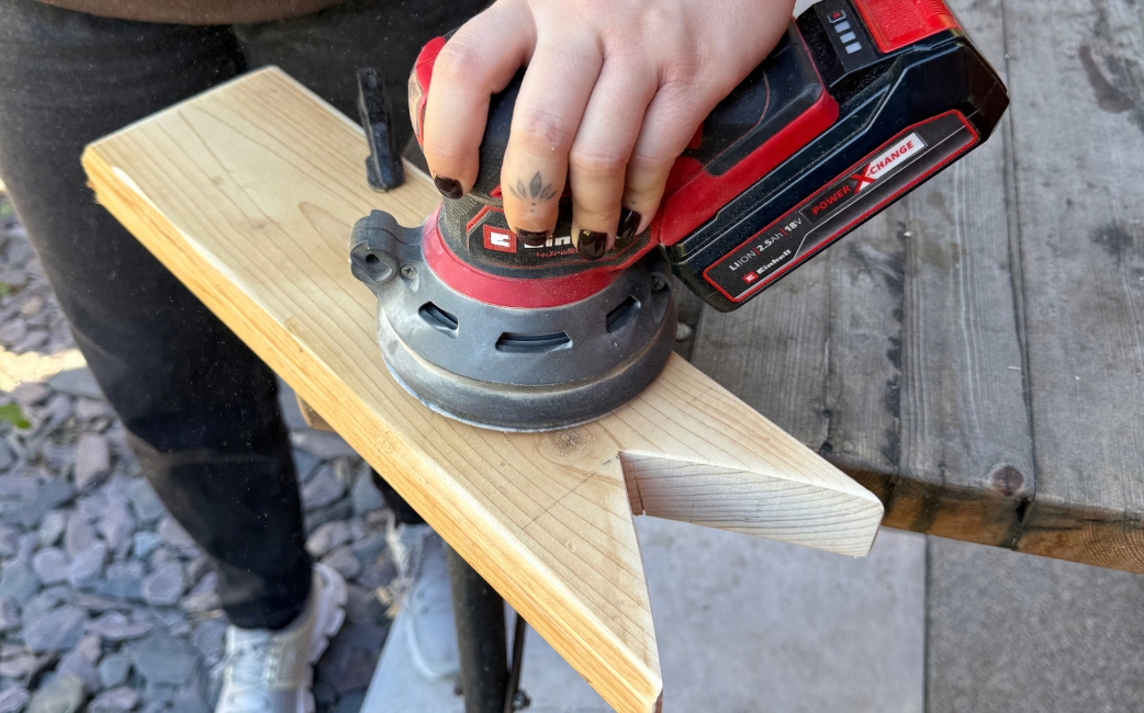 Eine Person bearbeitet ein Holzbrett mit einem Akku-Exzenterschleifer.