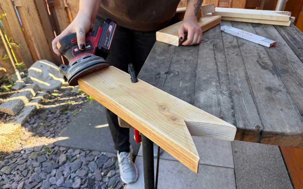 Eine Person schleift ein zugeschnittenes Holzbrett mit einem Akku-Exzenterschleifer.