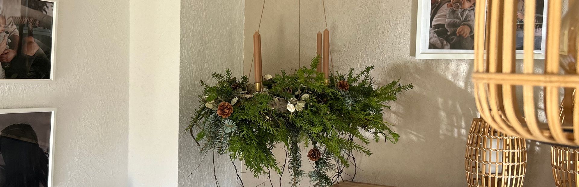 Ein hängender Adventskranz aus Tannengrün mit vier braunen Stabkerzen, verziert mit Zapfen und Trockenpflanzen.