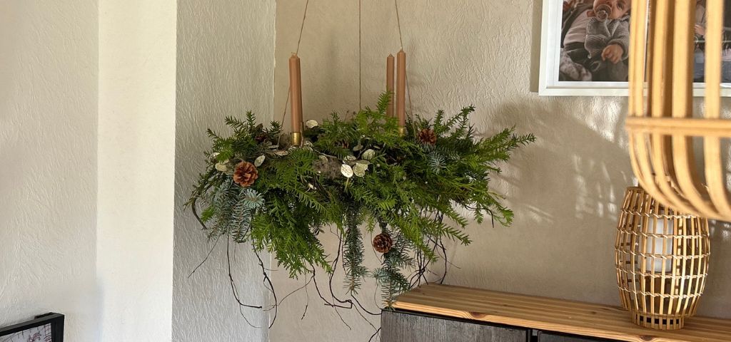 Ein hängender Adventskranz aus Tannengrün mit vier braunen Stabkerzen, verziert mit Zapfen und Trockenpflanzen.