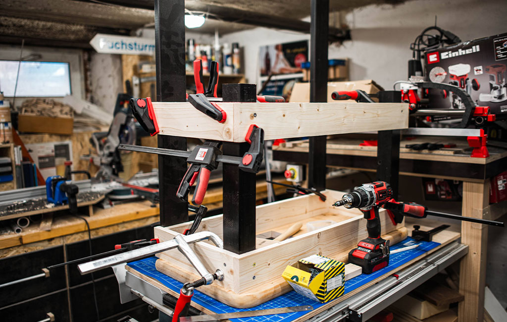 Die Holzkonstruktion der Matschküche ist eingespannt und wird mit Schrauben befestigt.