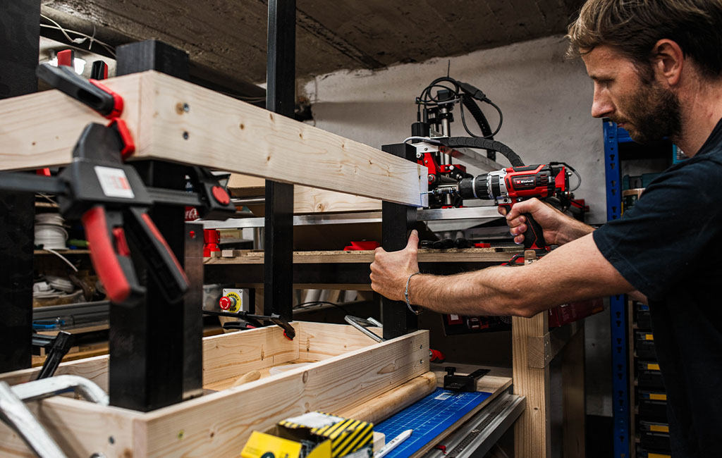 Ein Mann befestigt die obere Rahmenkonstruktion der Matschküche mit einem Akkuschrauber.