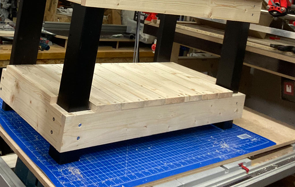 Der untere Boden der Matschküche aus Holz ist mit schwarzen Tischbeinen montiert.