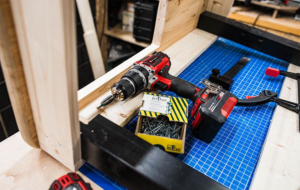 Akkuschrauber, Schraubenbox und Schraubzwinge liegen auf dem Holzkorpus der Matschküche.