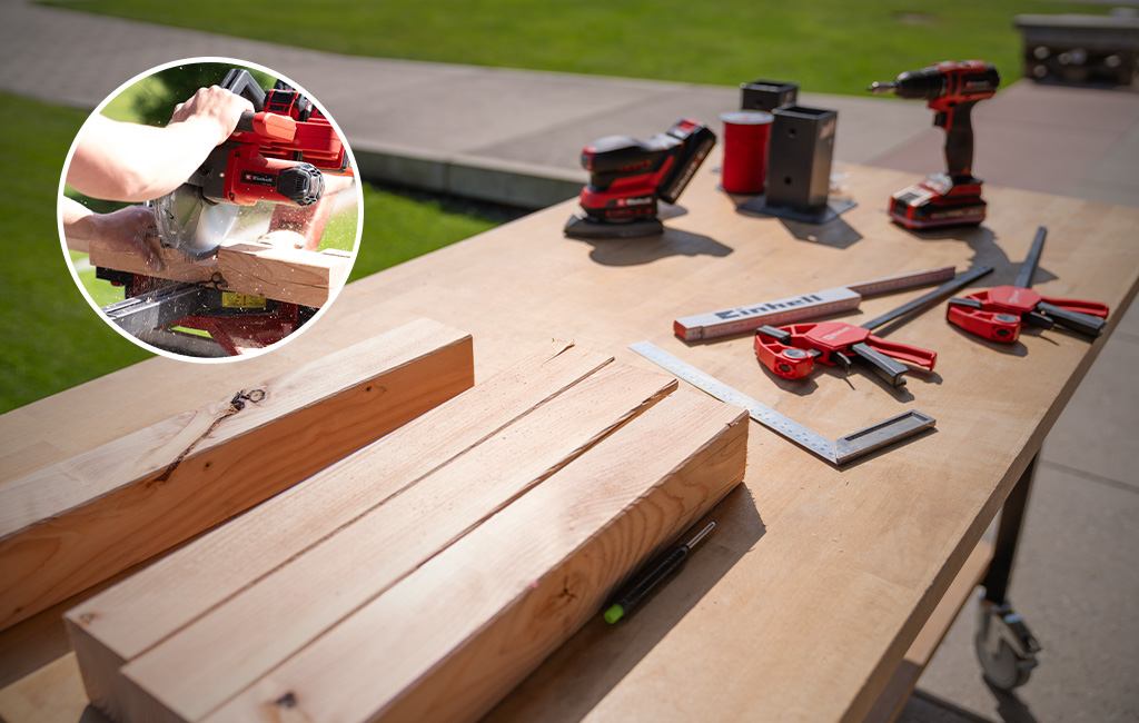 Auf einem Arbeitstisch liegen zugeschnittene Holzbalken, Werkzeuge, Einhell Geräte und ein runder Ausschnitt zeigt das Sägen von Holz.