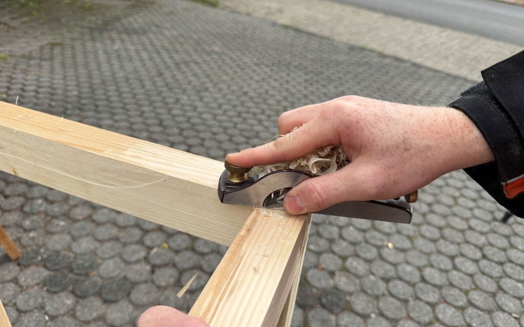 Eine Hand glättet eine Holzverbindung am Rahmen des Pflanztisches mit einem Einhandhobel.