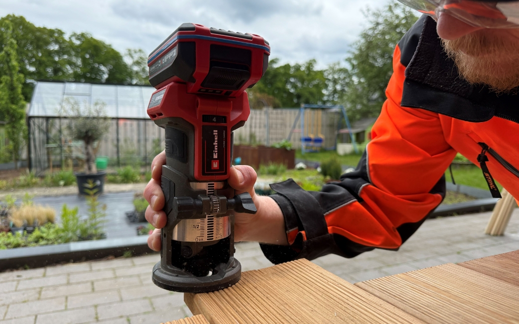Eine Person rundet die Kanten der Terrassendielen für die Tischplatte mit einer Akku-Kantenfräse ab.