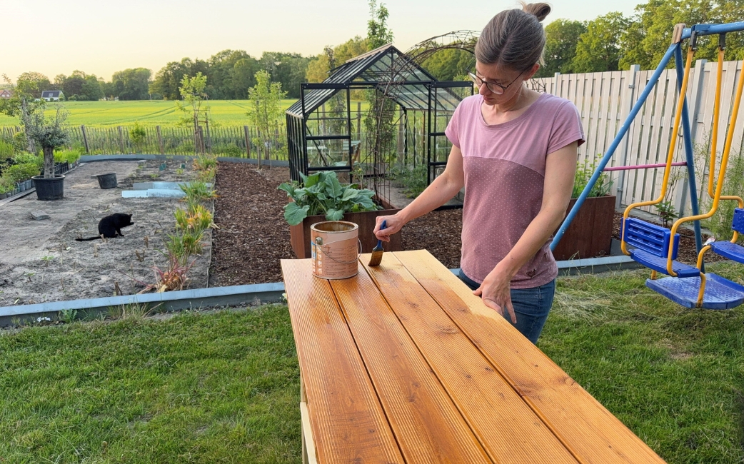 Eine Frau streicht die Rückwand des Pflanztisches im Garten mit Holzöl.