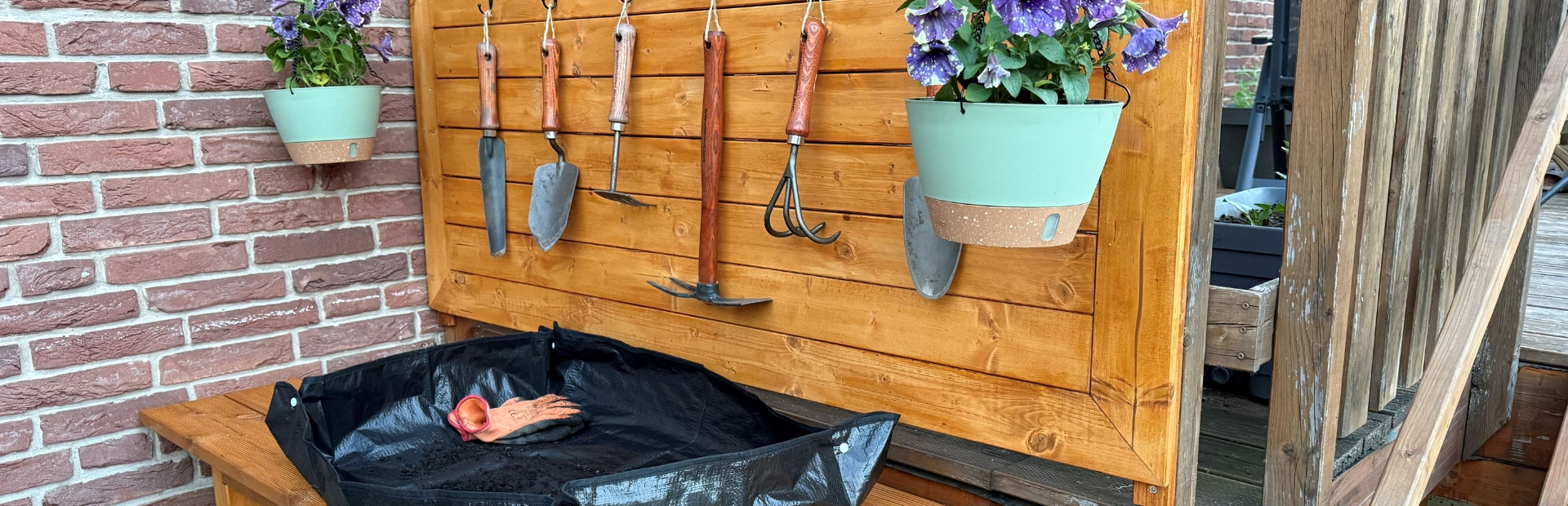 Ein fertig dekorierter Pflanztisch mit Rückwand, Gartenwerkzeugen, Blumenampel und Pflanzunterlage.