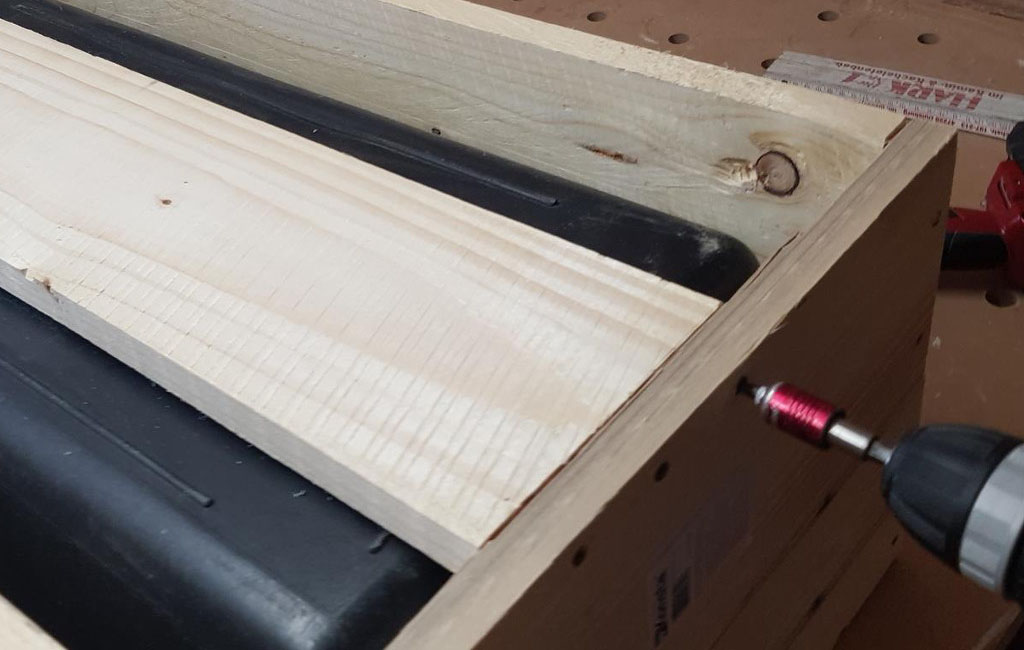 A wooden slat is screwed to a wooden box, next to it is the black plastic box.